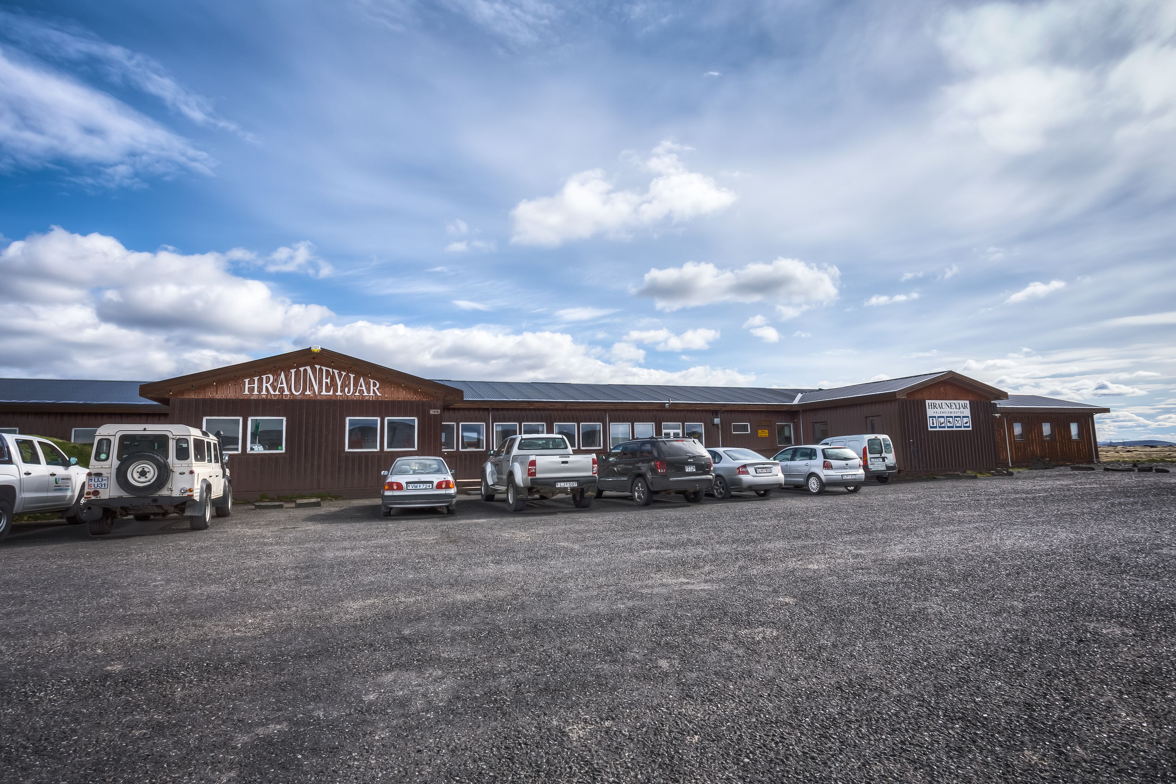 A building with a sign reading "HRAUNEYAR" and a parking lot with several vehicles.