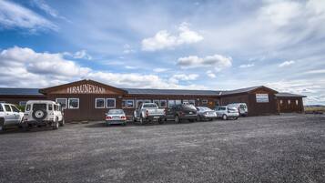A building with a sign reading "HRAUNEYAR" and a parking lot with several vehicles.