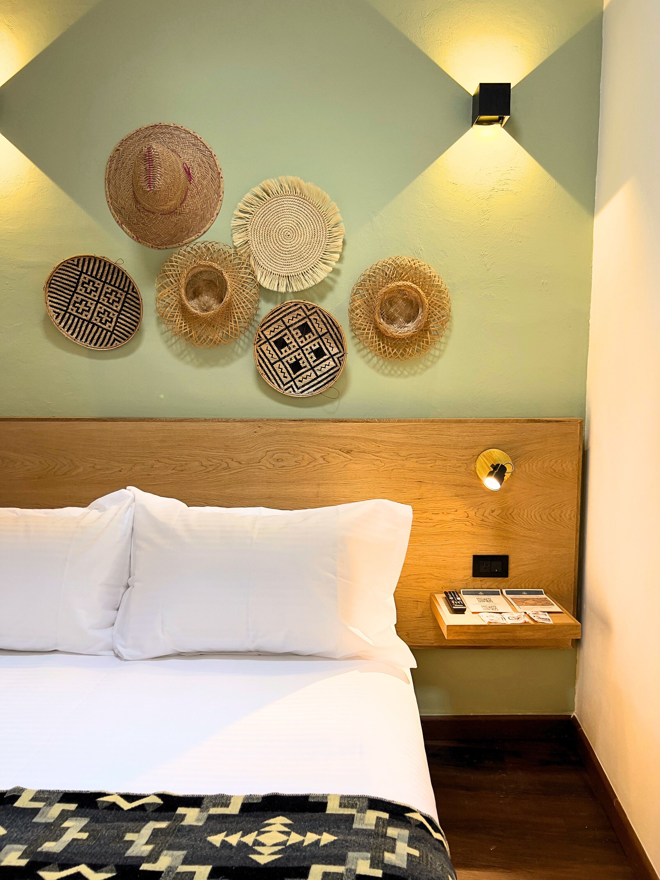 Una cama con ropa de cama blanca, un cabecero de madera y una mesita de noche con un control remoto y folletos.