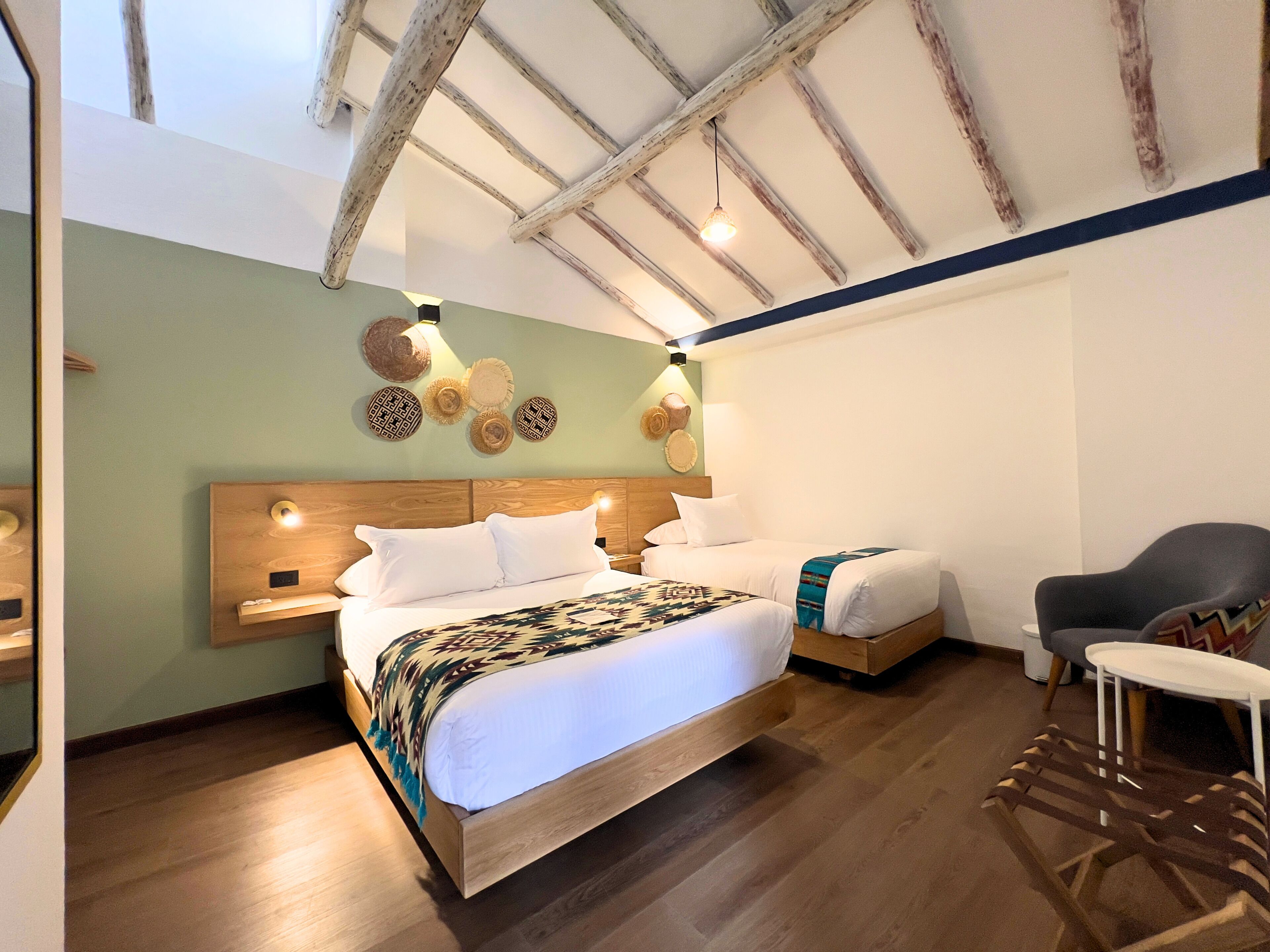 A room with a wooden ceiling, a bed with a patterned blanket, a chair, and wall decor.