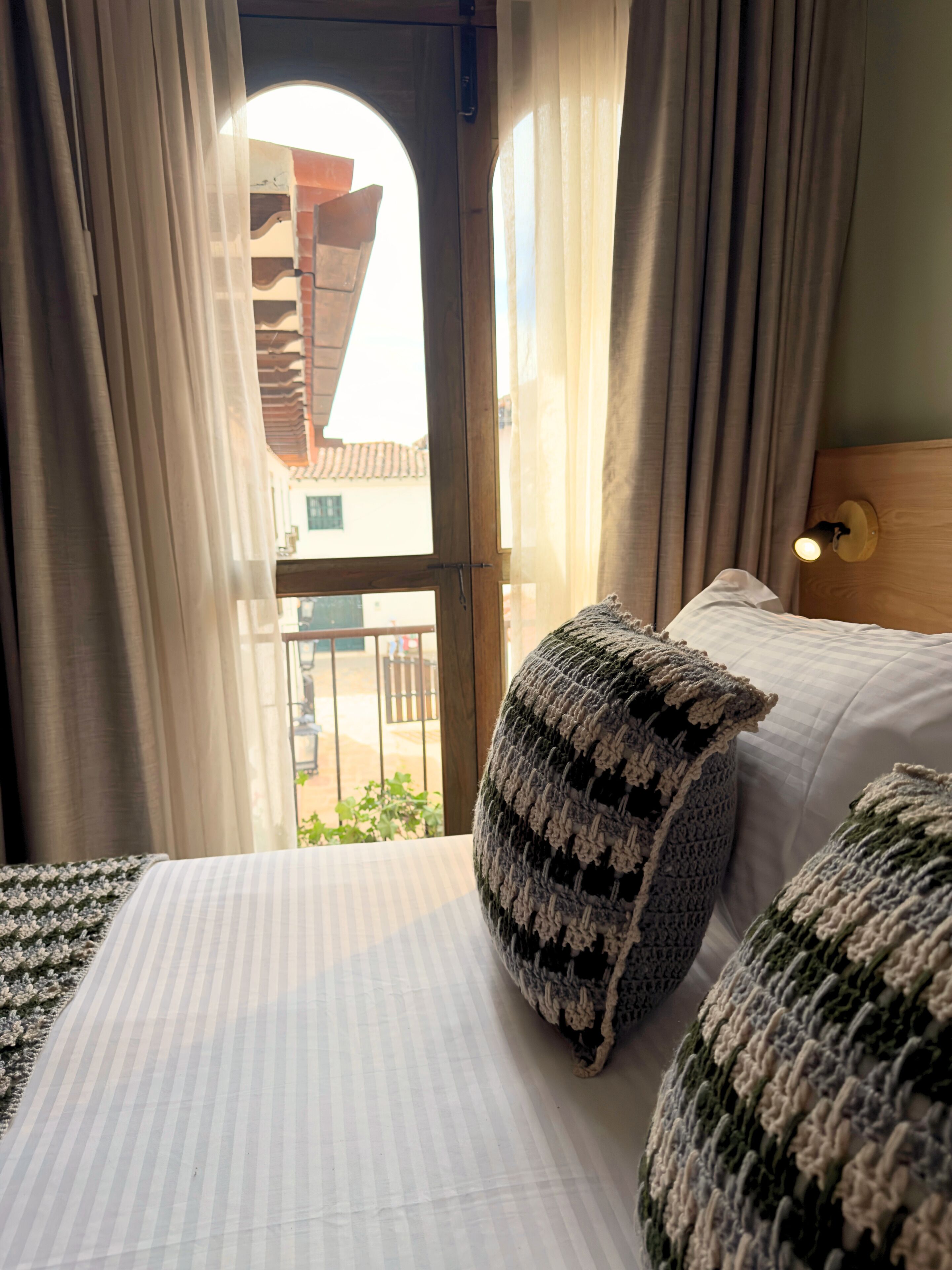 Una habitación de hotel con una cama, una ventana con cortinas y vistas a edificios.