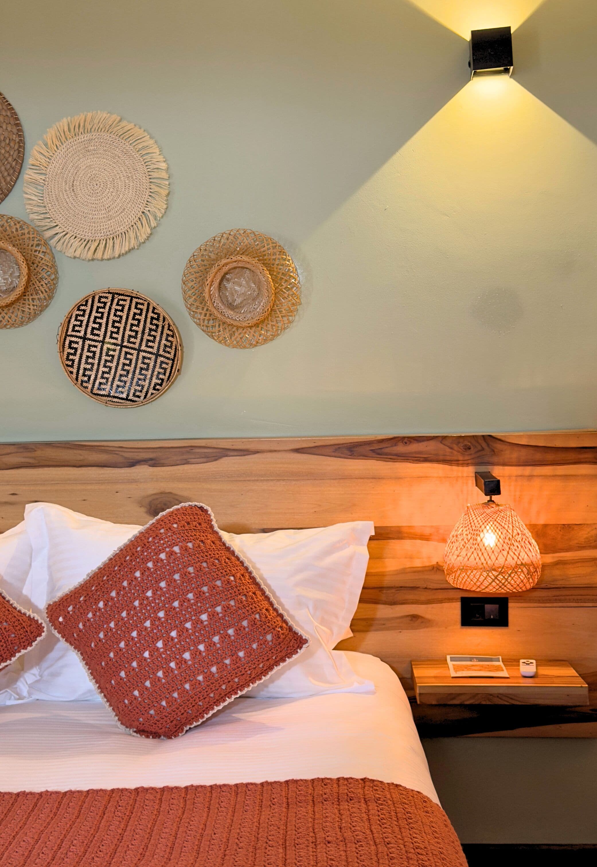 Ein Bett mit Holz-Kopfseitenverkleidung, ein Nachttisch mit Lampe sowie Wanddekoration, darunter gewebte Körbe.
