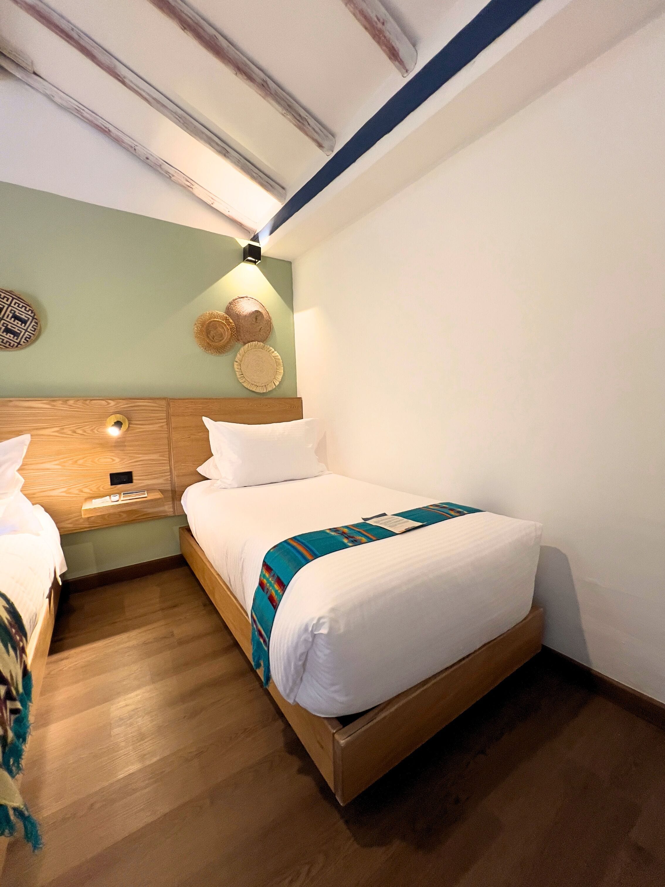 A hotel room with a wooden bed, a nightstand, and a wall-mounted lamp.