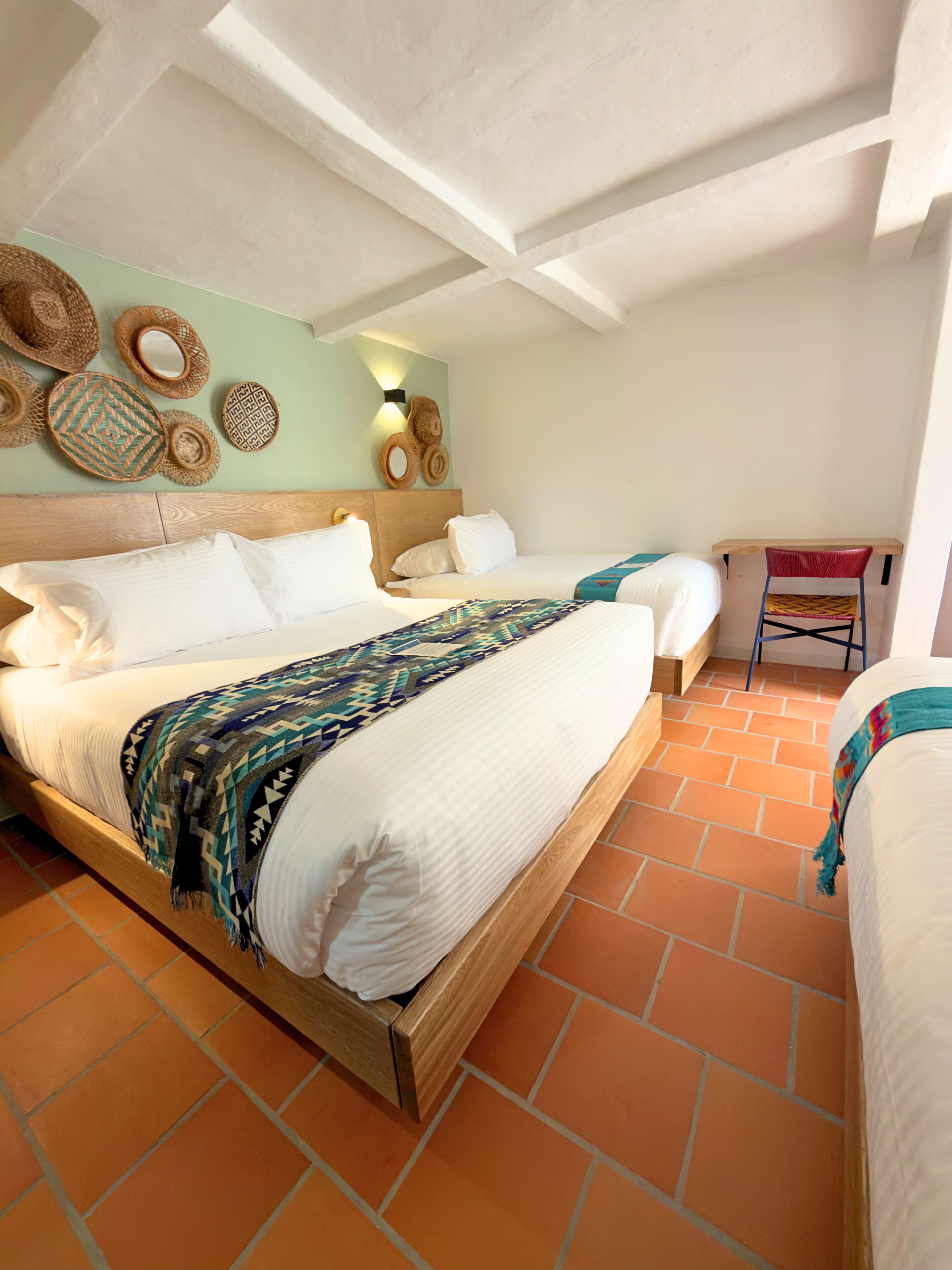 Habitación de hotel con una cama grande, cabecera de madera, luz instalada en la pared y una mesita con una silla.