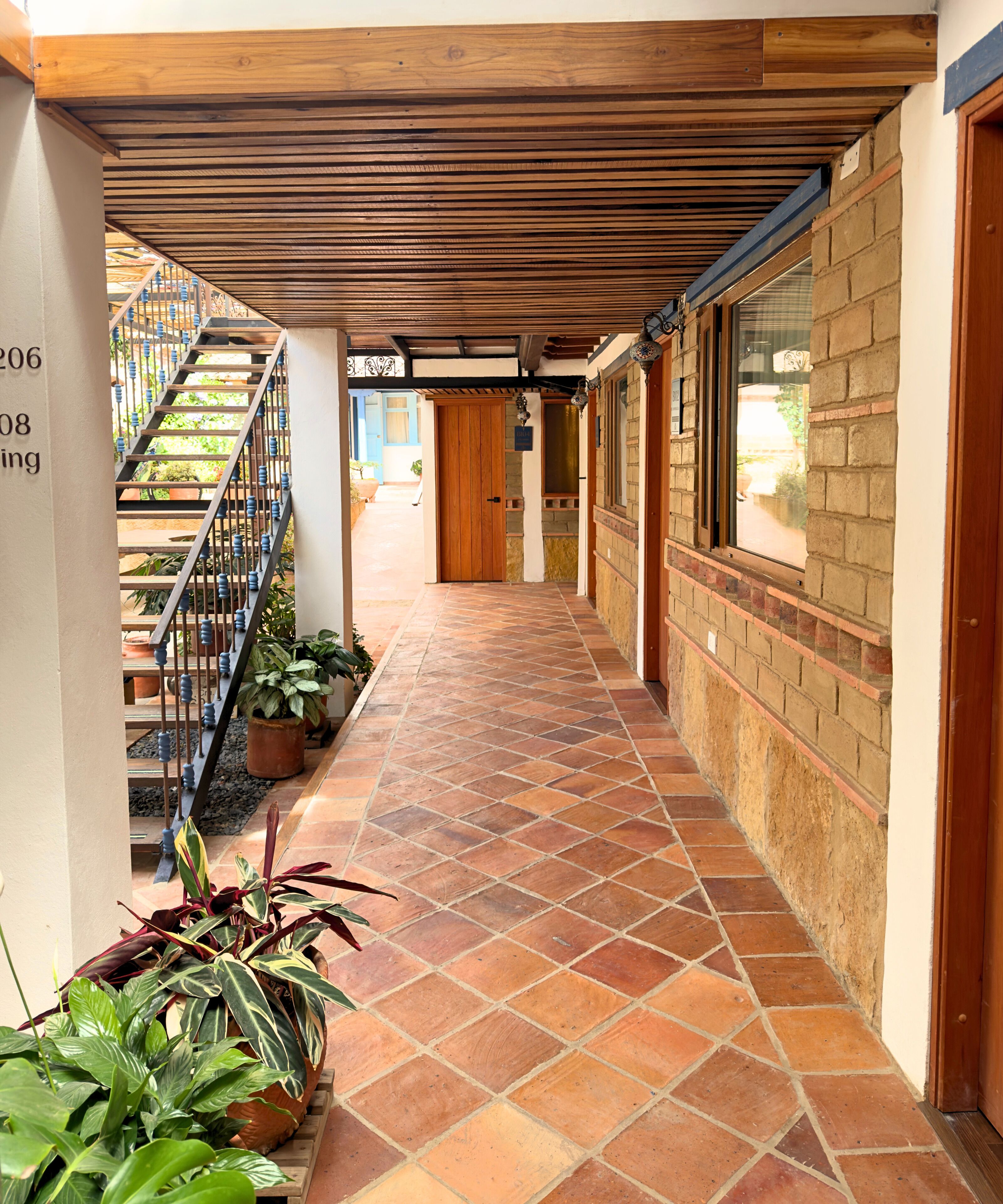 A corridor with a tiled floor, a wooden ceiling, and a staircase with blue railings.