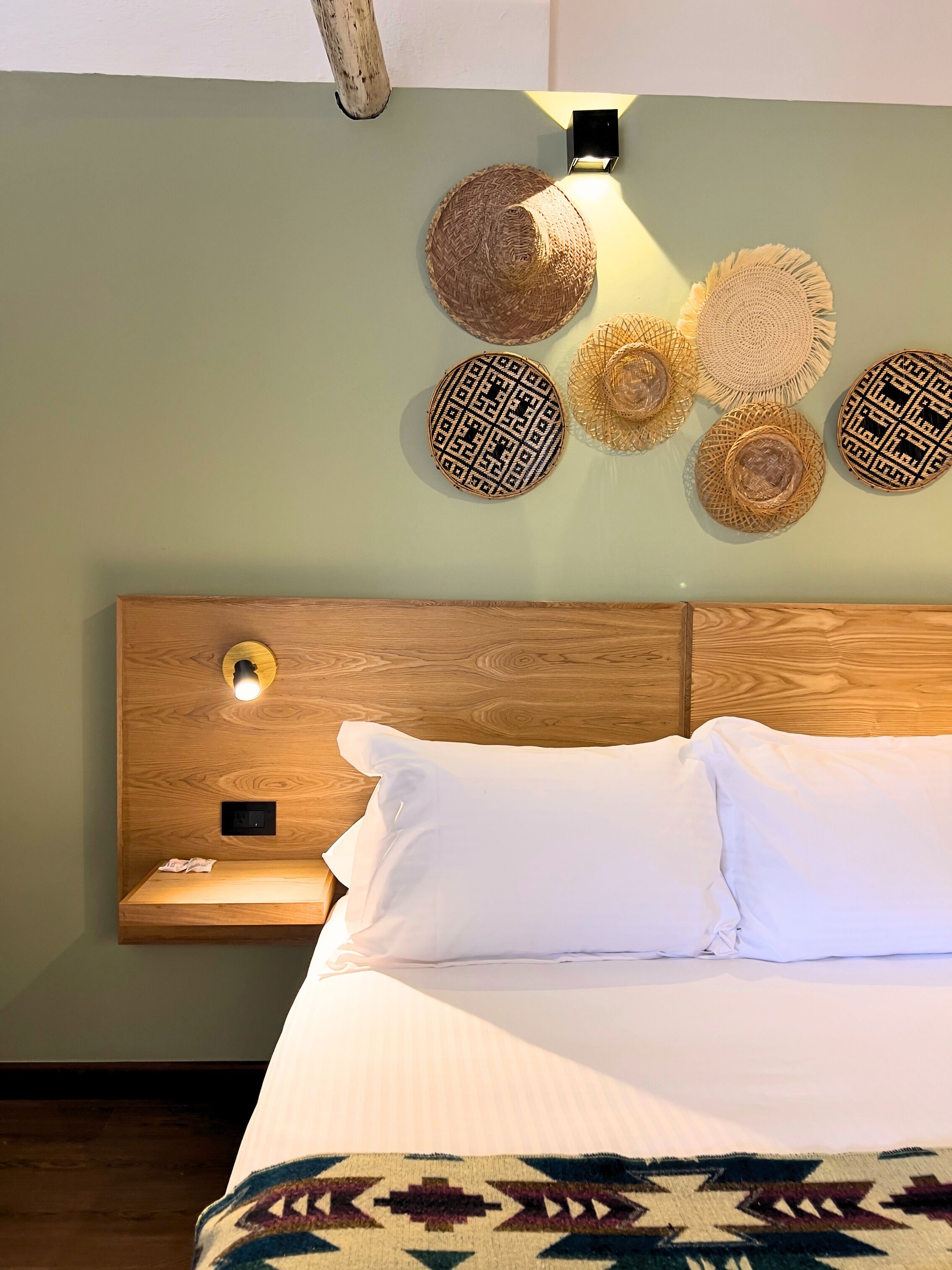A neatly made bed with white linens, a wooden headboard, and a wall-mounted light fixture.