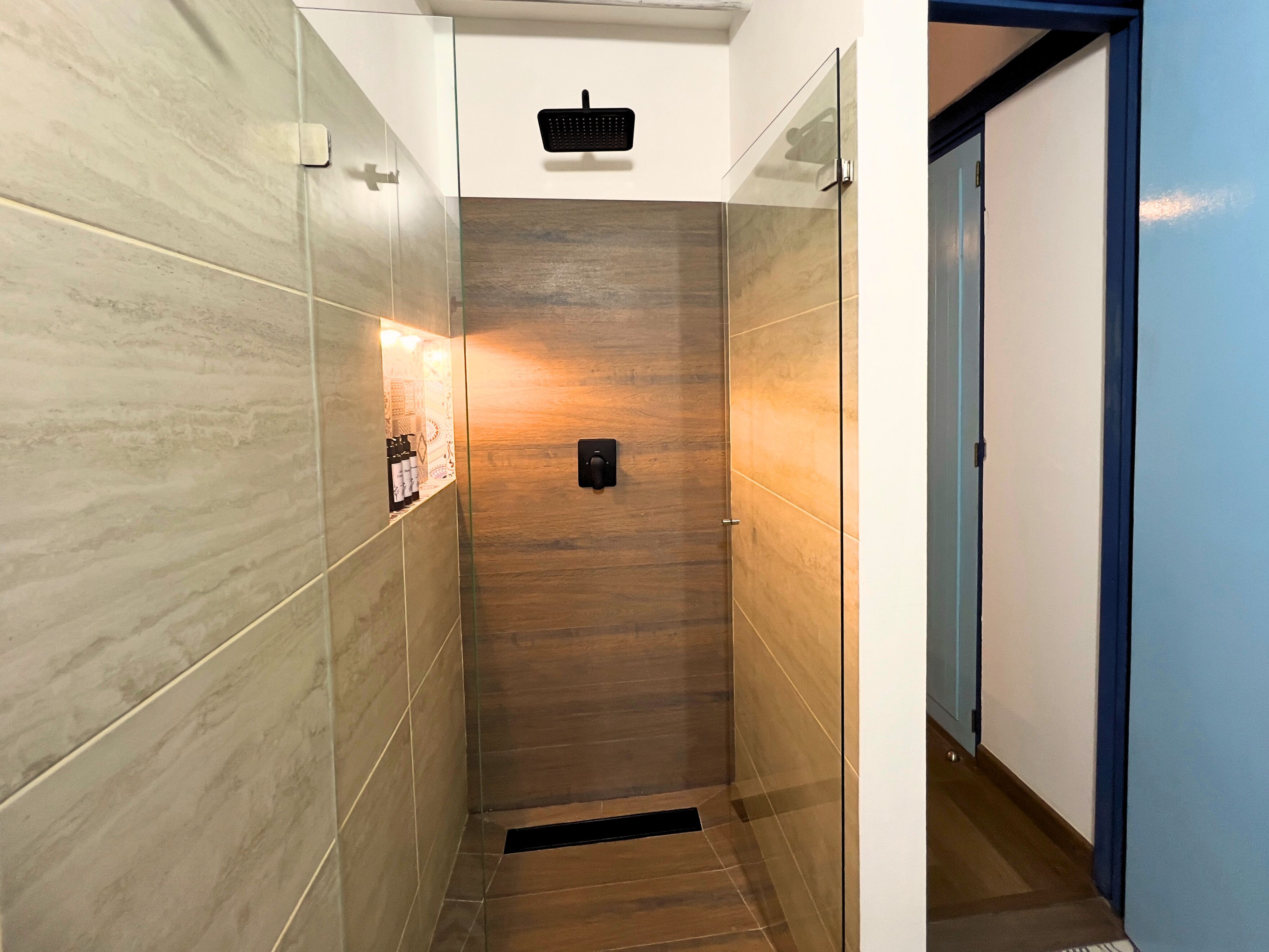 A narrow hallway with tiled walls and a wooden floor, leading to a door.