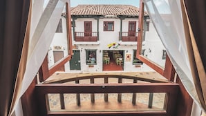 A view from a balcony with a wooden railing, looking out at a building with a tiled roof and multiple windows. - Casa Sie (Villa de Leyva)