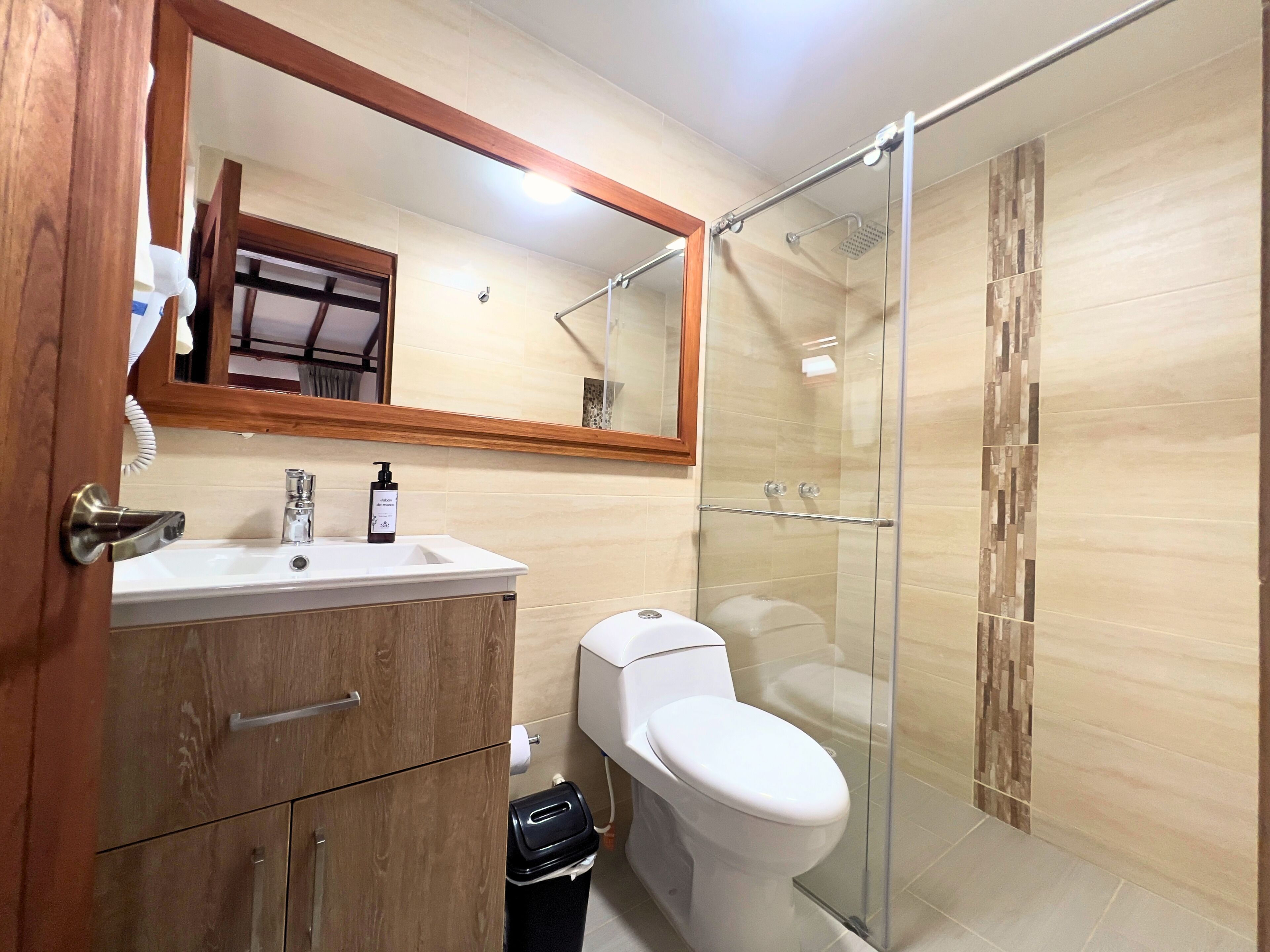 A modern bathroom with a wooden vanity, a toilet, a glass shower enclosure, and a large mirror.