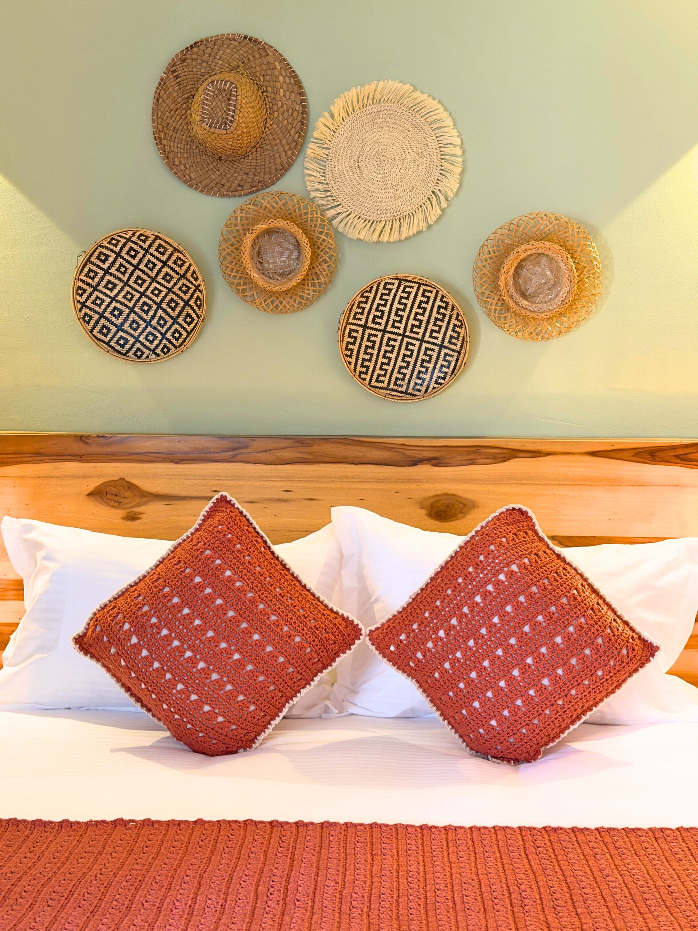 Una cama con dos almohadas cuadradas y un tapiz tejido en la pared.