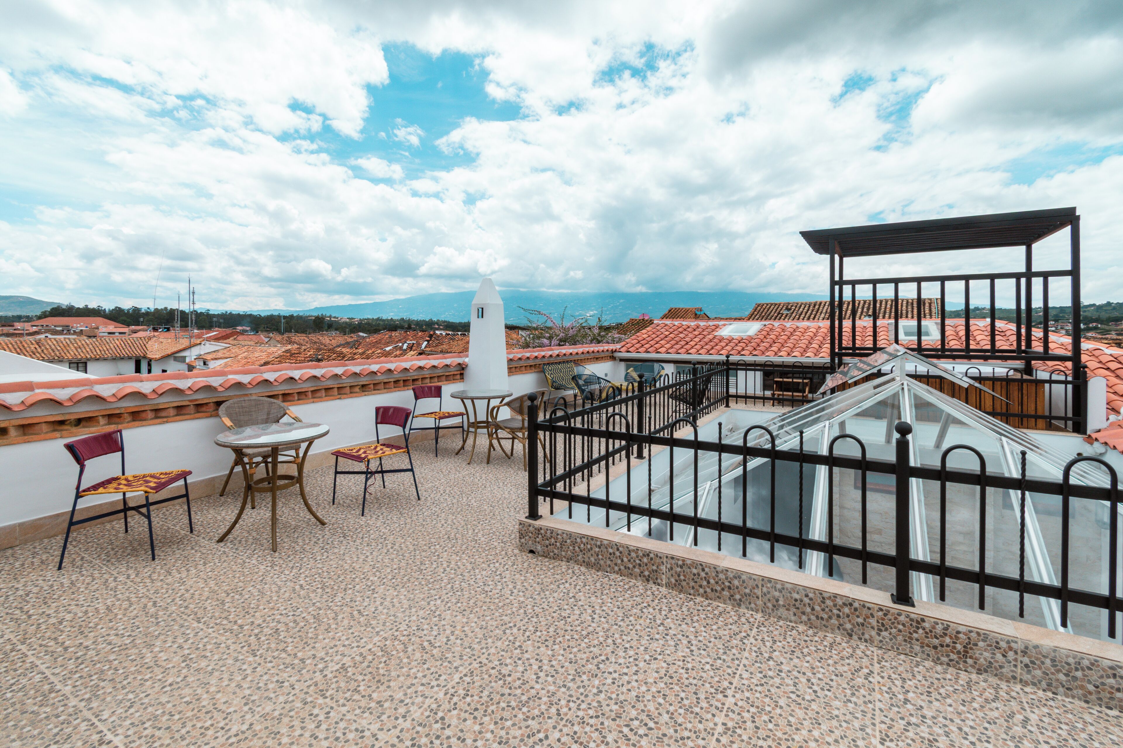 Une terrasse sur le toit, dotée d’un sol carrelé, d’une petite table avec des chaises, d’une rambarde en métal et offrant une vue sur le paysage urbain.