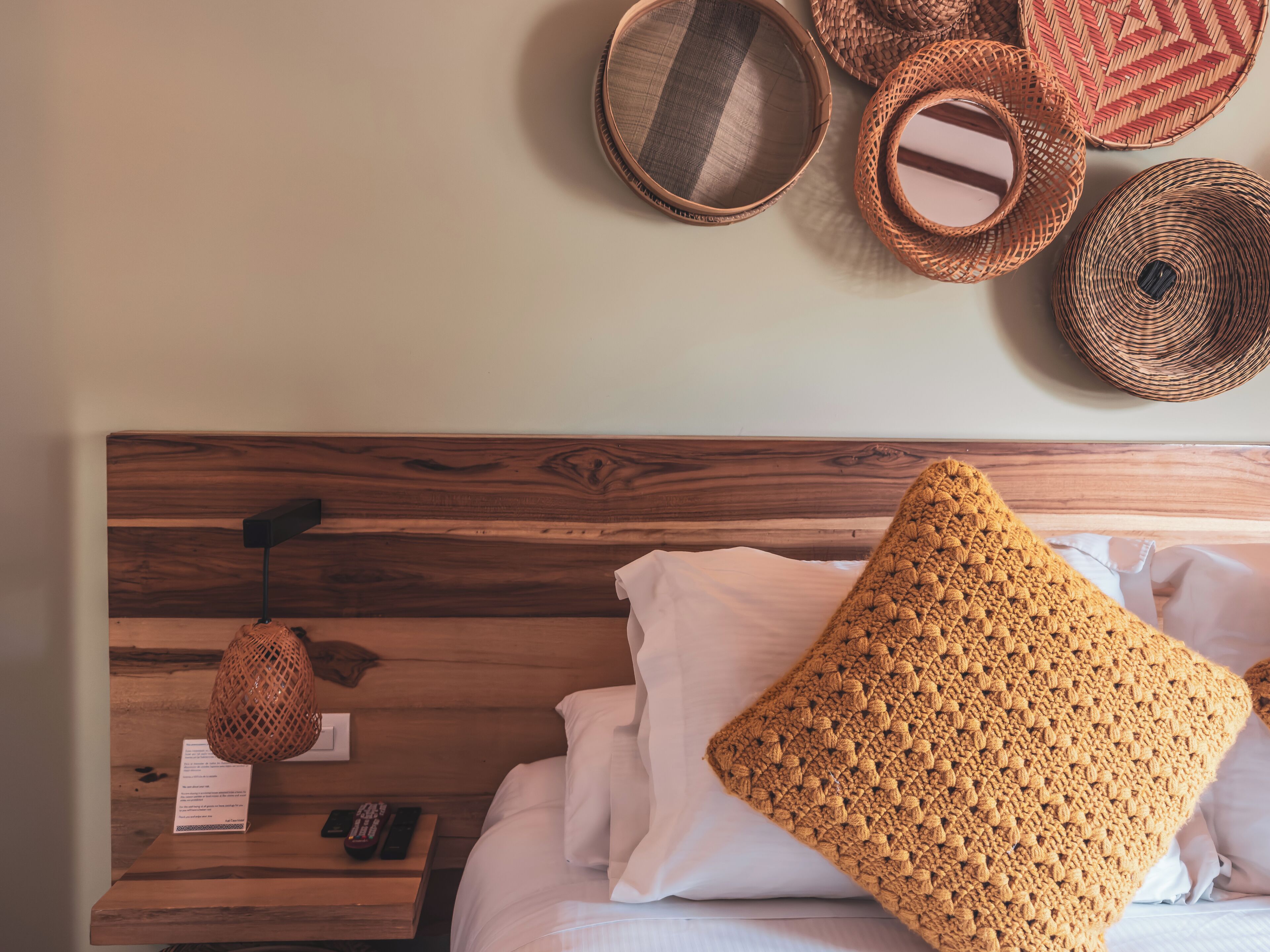 Una cama bien hecha con sábanas blancas, cabecera de madera y un cojín de crochet.