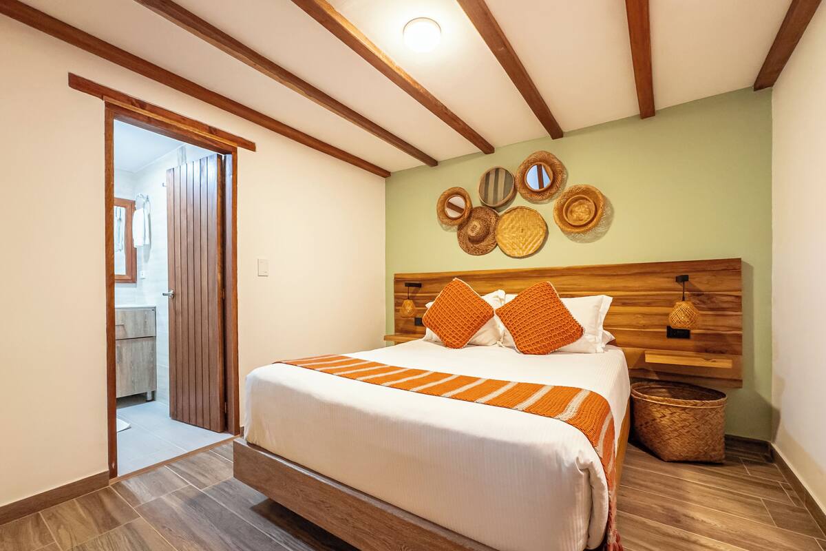 A bedroom with a bed, wooden beams, a wall-mounted light fixture, and a woven basket.