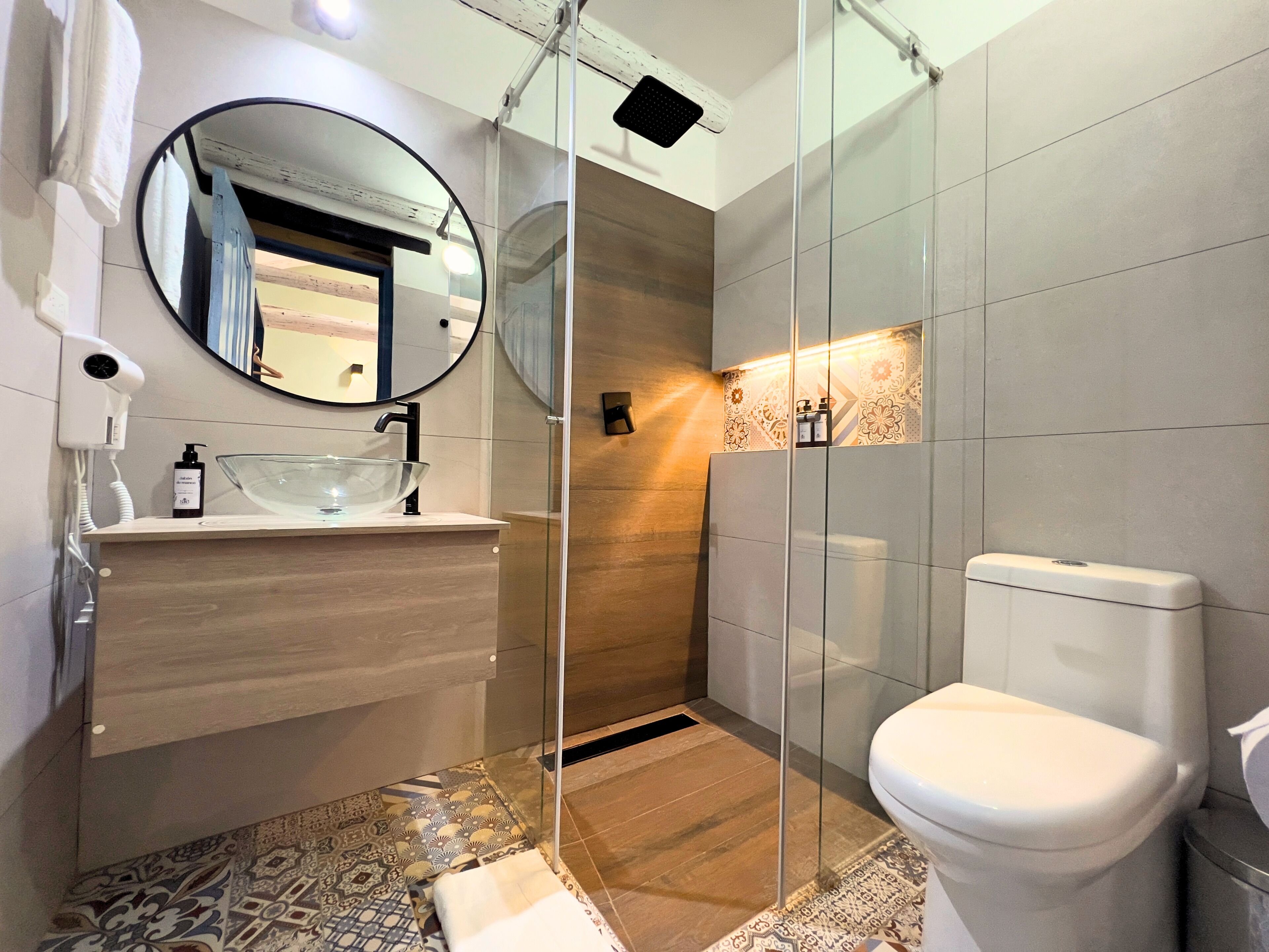 Un baño moderno con cabina de ducha de vidrio, un espejo redondo y un inodoro blanco.