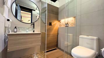 Un baño moderno con cabina de ducha de vidrio, un espejo redondo y un inodoro blanco.