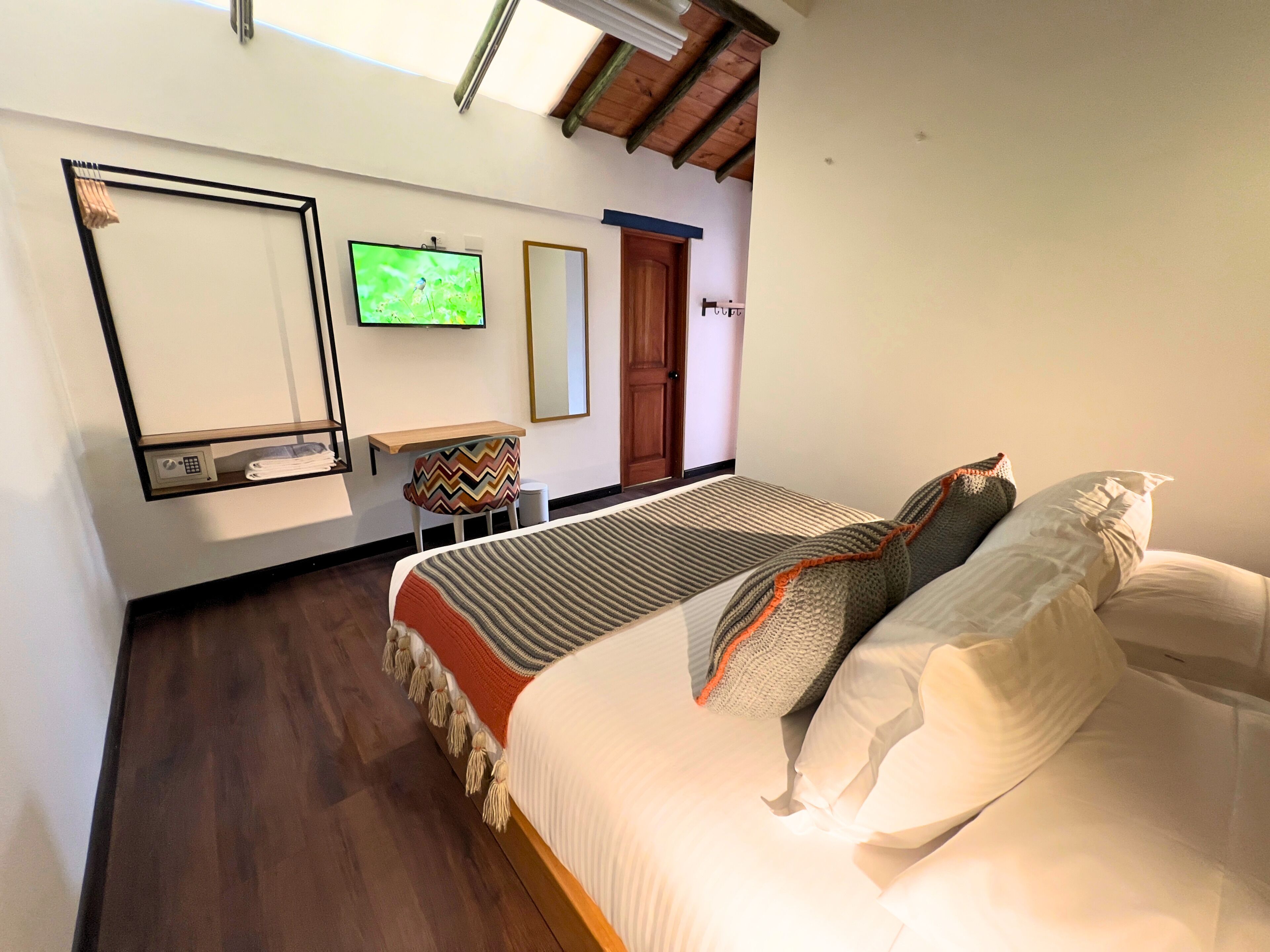 Una habitación de hotel con una cama, televisor en la pared, una mesita y una silla, y una puerta.