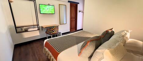 Una habitación de hotel con una cama, televisor en la pared, una mesita y una silla, y una puerta.