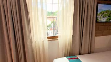 A hotel room with a bed, curtains, a window, and a television on the wall.