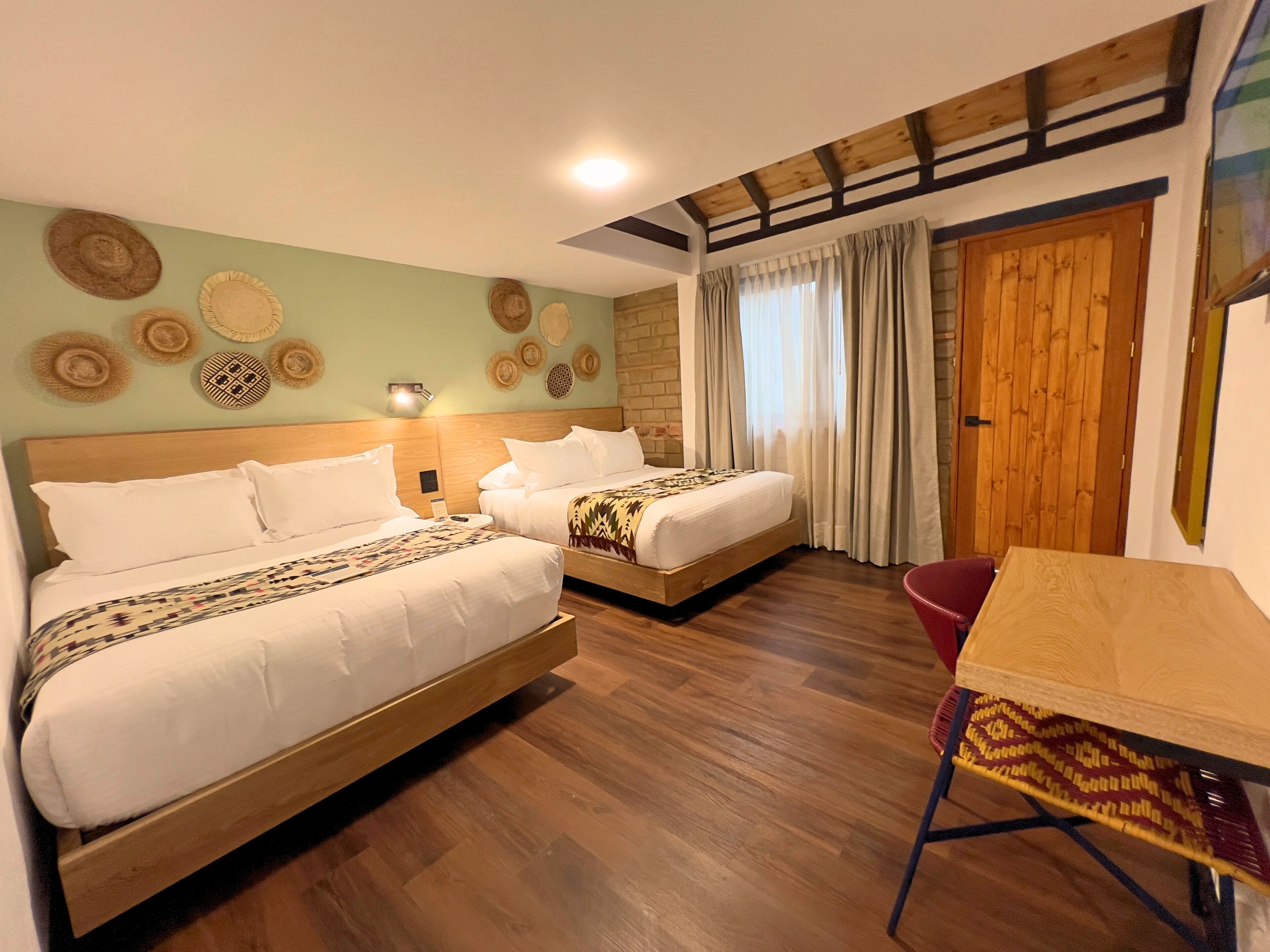 Une chambre d’hôtel avec deux lits, un plancher en bois, une table et un mur décoré de chapeaux tressés.
