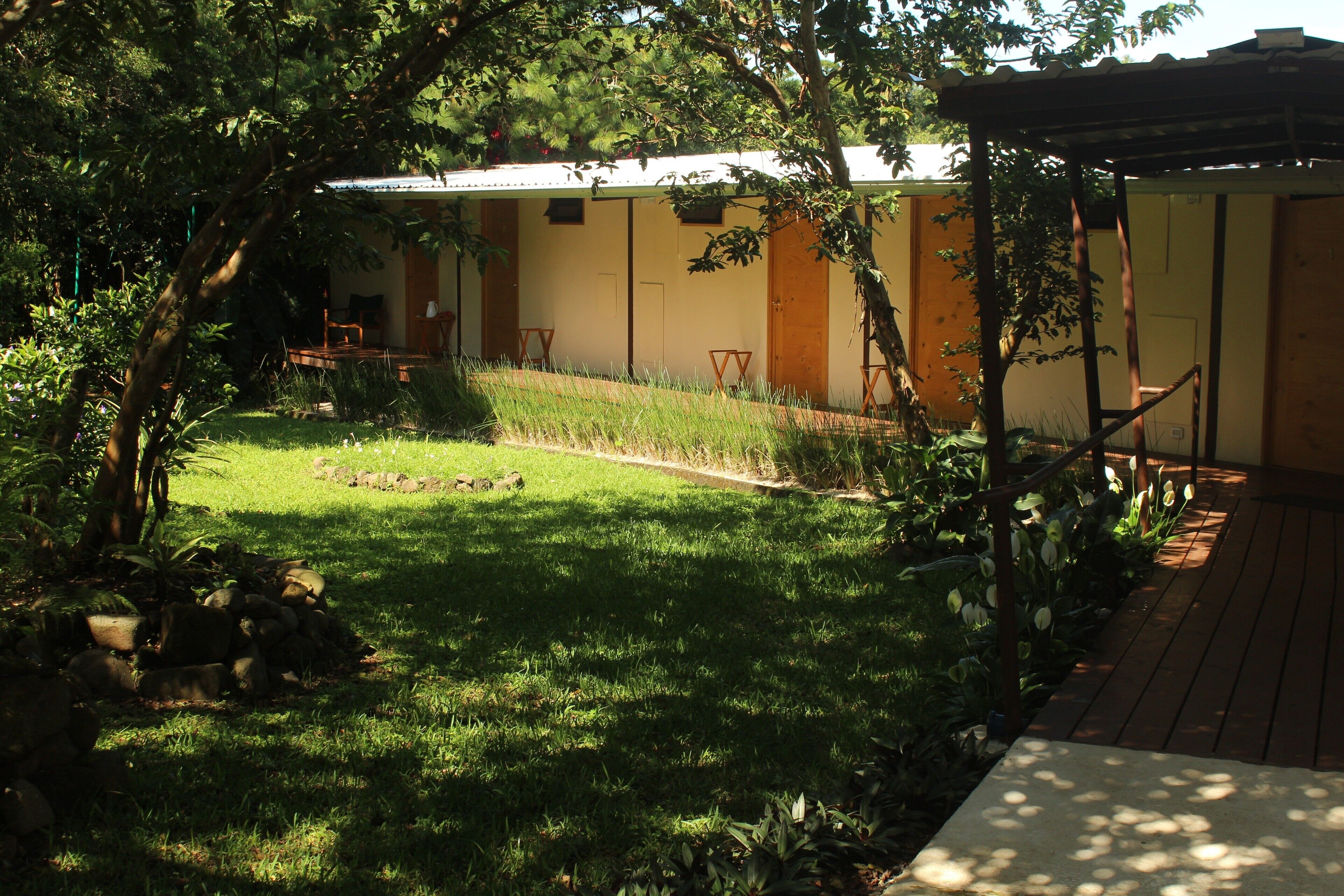 A garden with a wooden deck, a small lawn, and a building with a tiled roof.