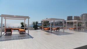 Una terrazza sul tetto con lettini prendisole e un pergolato, con vista sulla città costiera.