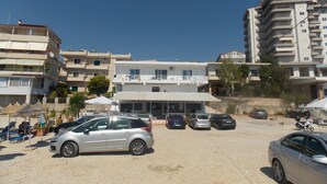 Un parcheggio con diverse auto, un edificio con facciata bianca e balconi, e un cielo azzurro intenso.