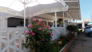 Un ristorante con posti a sedere all'aperto, coperto da ombrelloni bianchi e circondato da cespugli di rose.