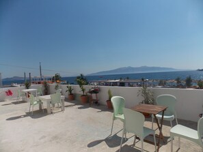 Una terraza en la azotea con mobiliario exterior, plantas en macetas y vistas al mar y a las montañas.