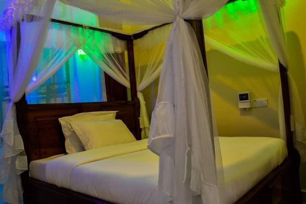 Una cama con dosel, cabecera de madera y mesita de noche con lámpara.
