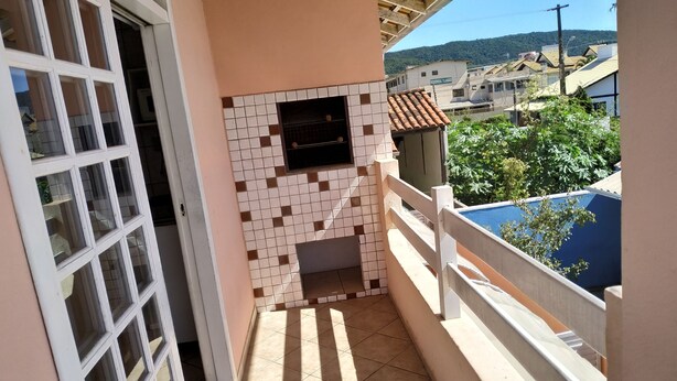 A balcony with a tiled wall, a small window, and a view of a residential area. - Residencial Praia Bombas (Bombinhas)