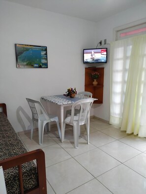 Una habitación pequeña y limpia con una mesa de comedor, dos sillas, un televisor y una ventana con cortinas.