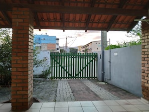 Una entrada protegida con un portón verde, pilares de ladrillo y un camino empedrado que conduce a un edificio con techo azul.