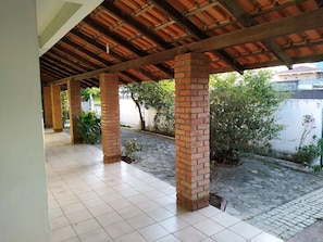 Un espacio exterior techado con piso de baldosas, pilares de ladrillo y plantas en macetas.