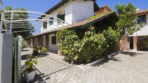 A residential building with a tiled roof, a covered porch, and a garden area with potted plants. - Residencial Praia Bombas (Bombinhas)