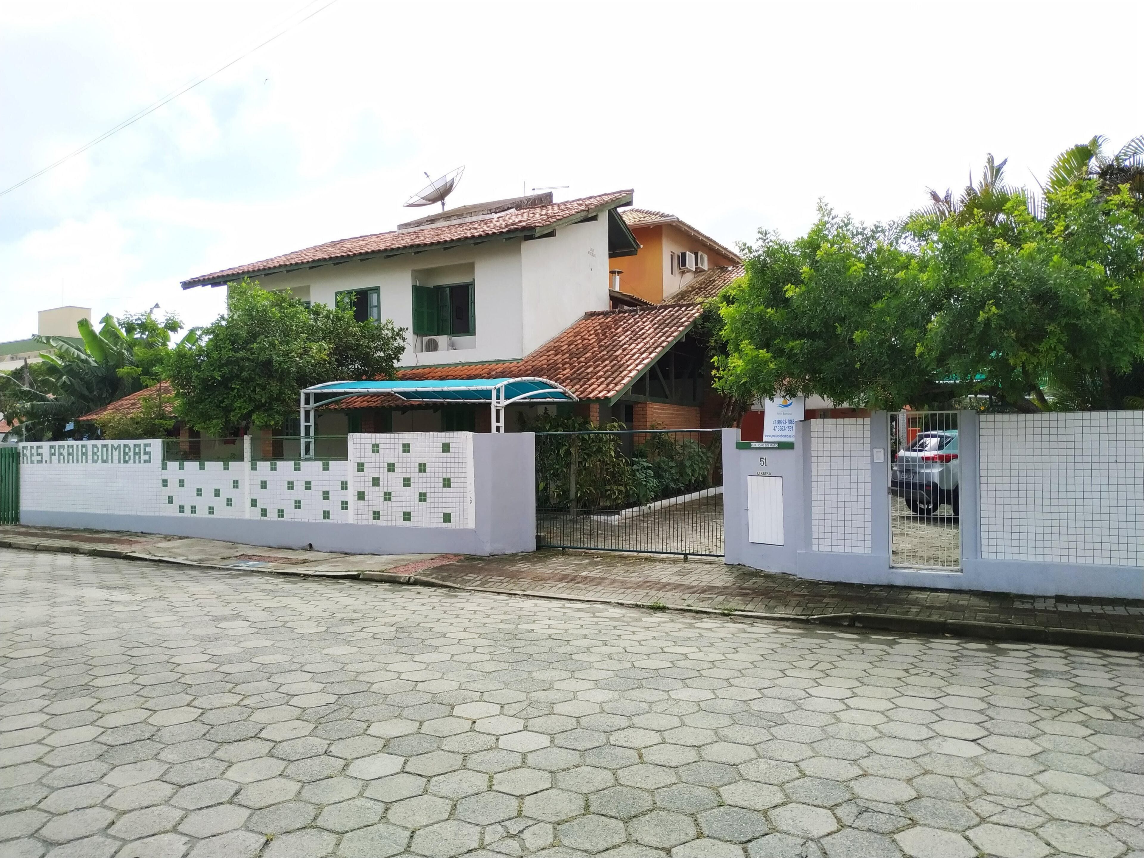 A two-story house with a tiled roof, a satellite dish, and a fenced yard.