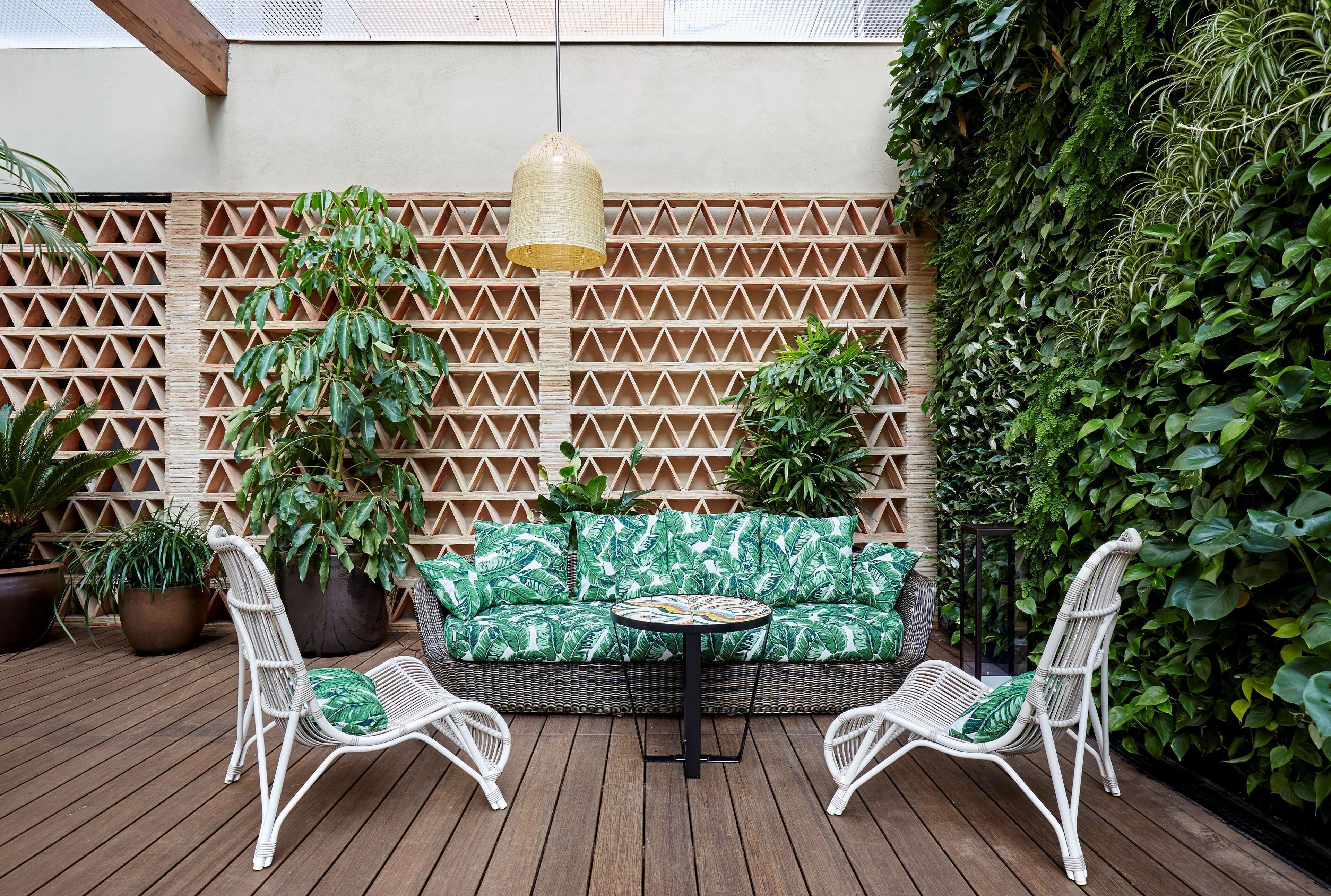 A wooden deck with a wicker sofa and two chairs, surrounded by potted plants and a lattice wall.