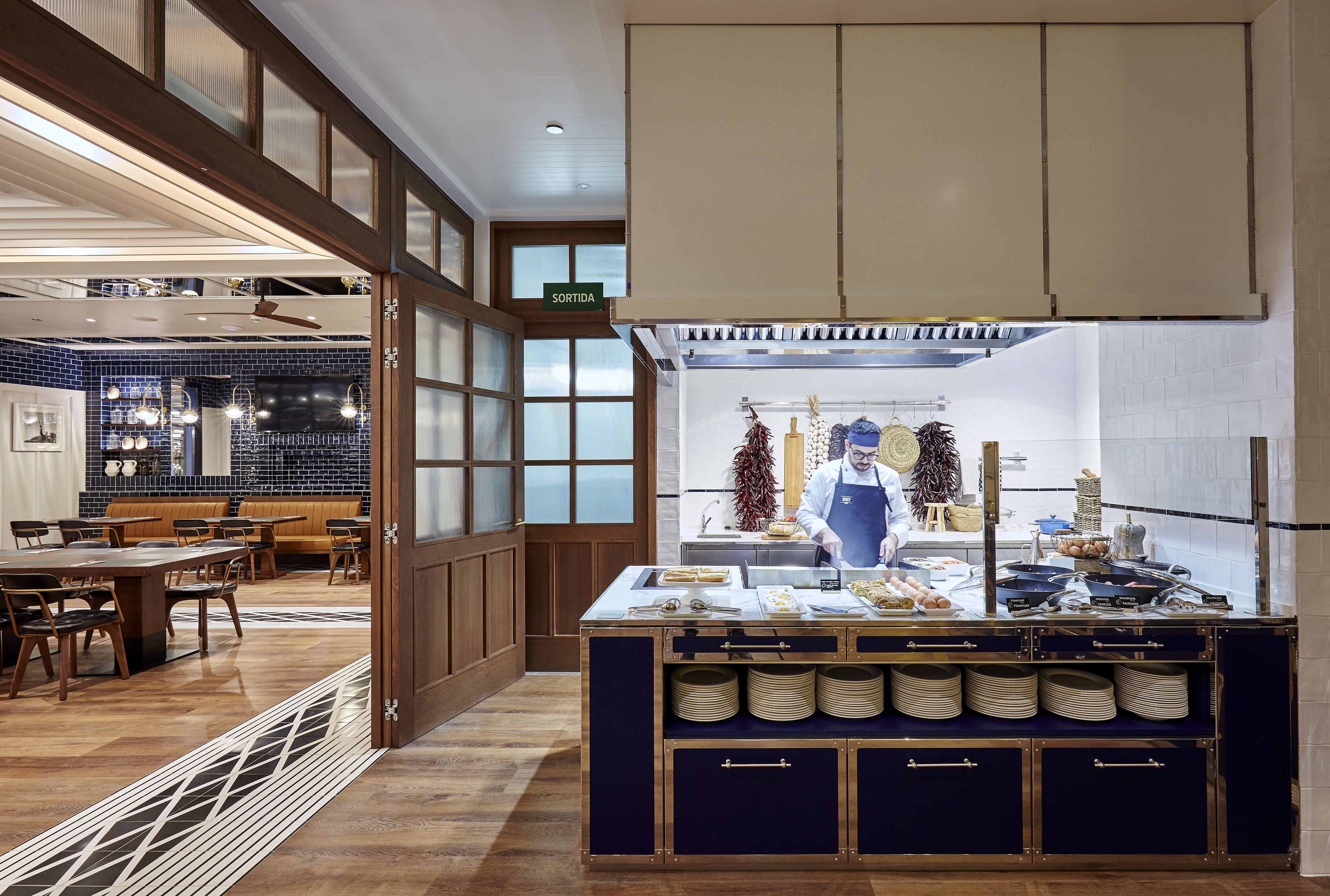 A restaurant with a counter, dining area, and kitchen visible.