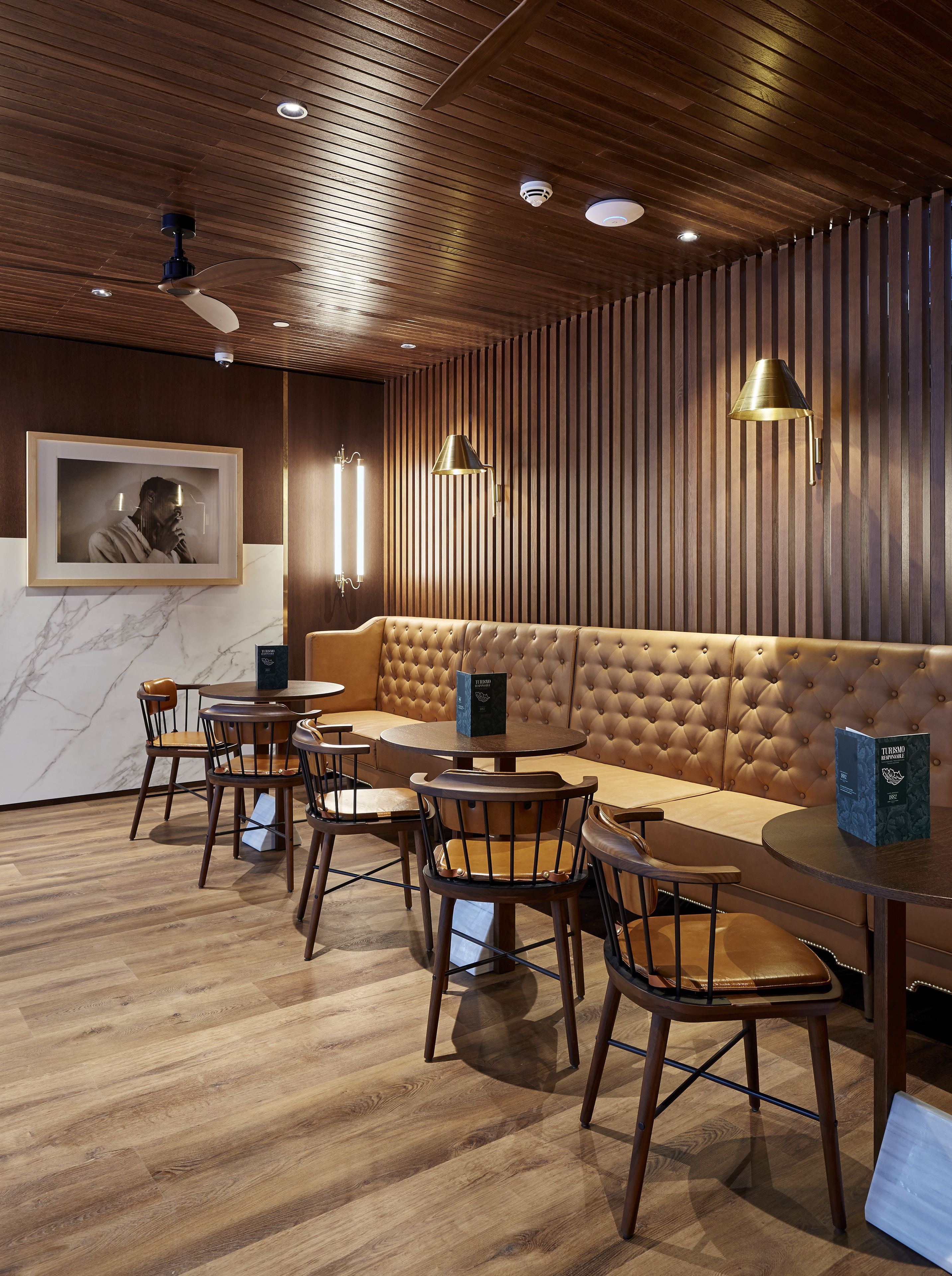 Interior de restaurante con paneles de madera, una banqueta de cuero acolchada y una pared de mármol con una fotografía enmarcada.