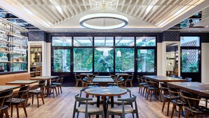A restaurant with round tables and chairs, a wooden ceiling, and large windows with a view of greenery. - Radisson Blu 1882 Hotel, Barcelona Sagrada Familia (Barcelona)