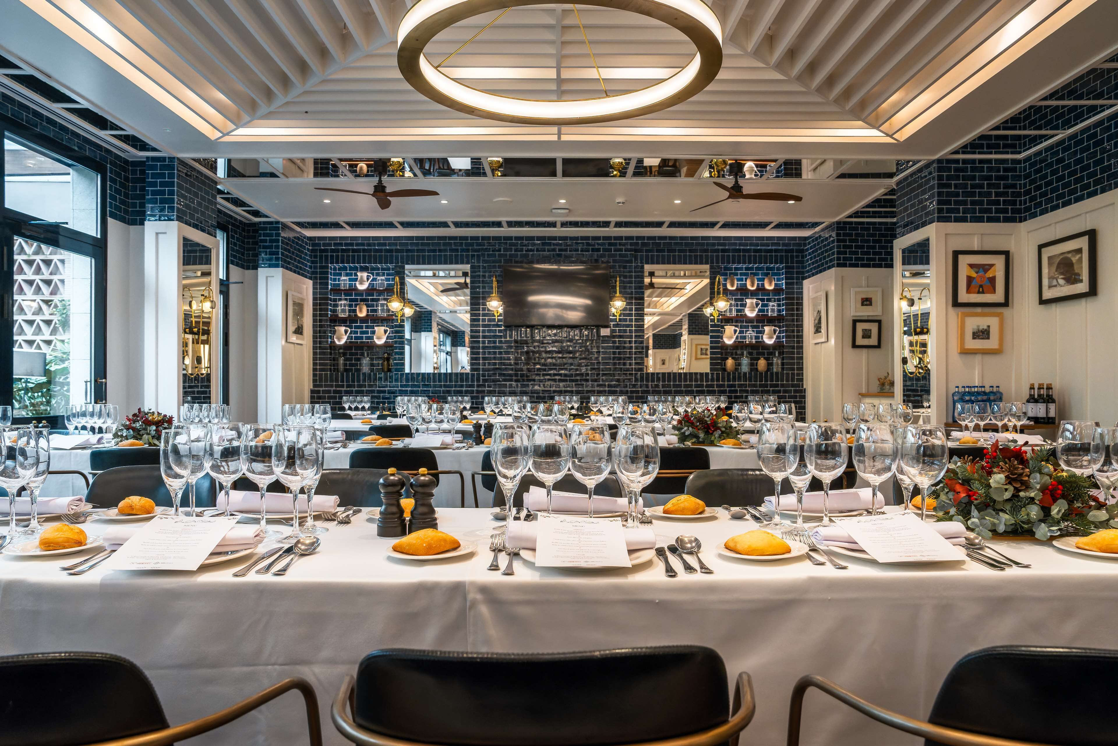 A restaurant with multiple tables set for dining, featuring white tablecloths, clear glassware, and neatly arranged cutlery.