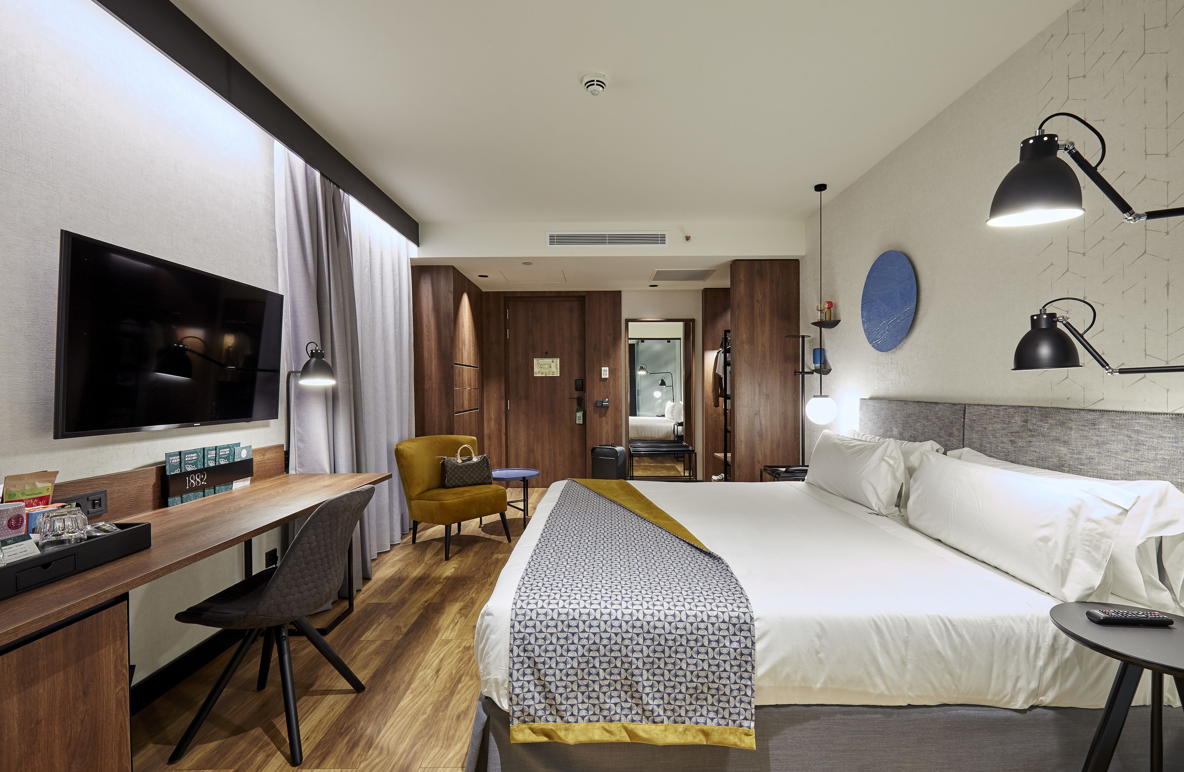 A hotel room with a large bed, a desk with a chair, a television, and a small table with a remote control.