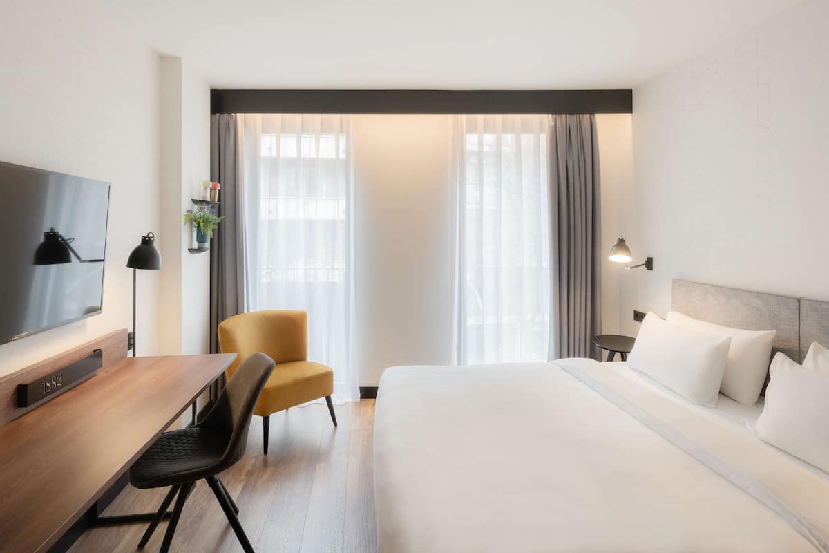 A hotel room with a bed, a desk, a chair, a TV, and curtains.