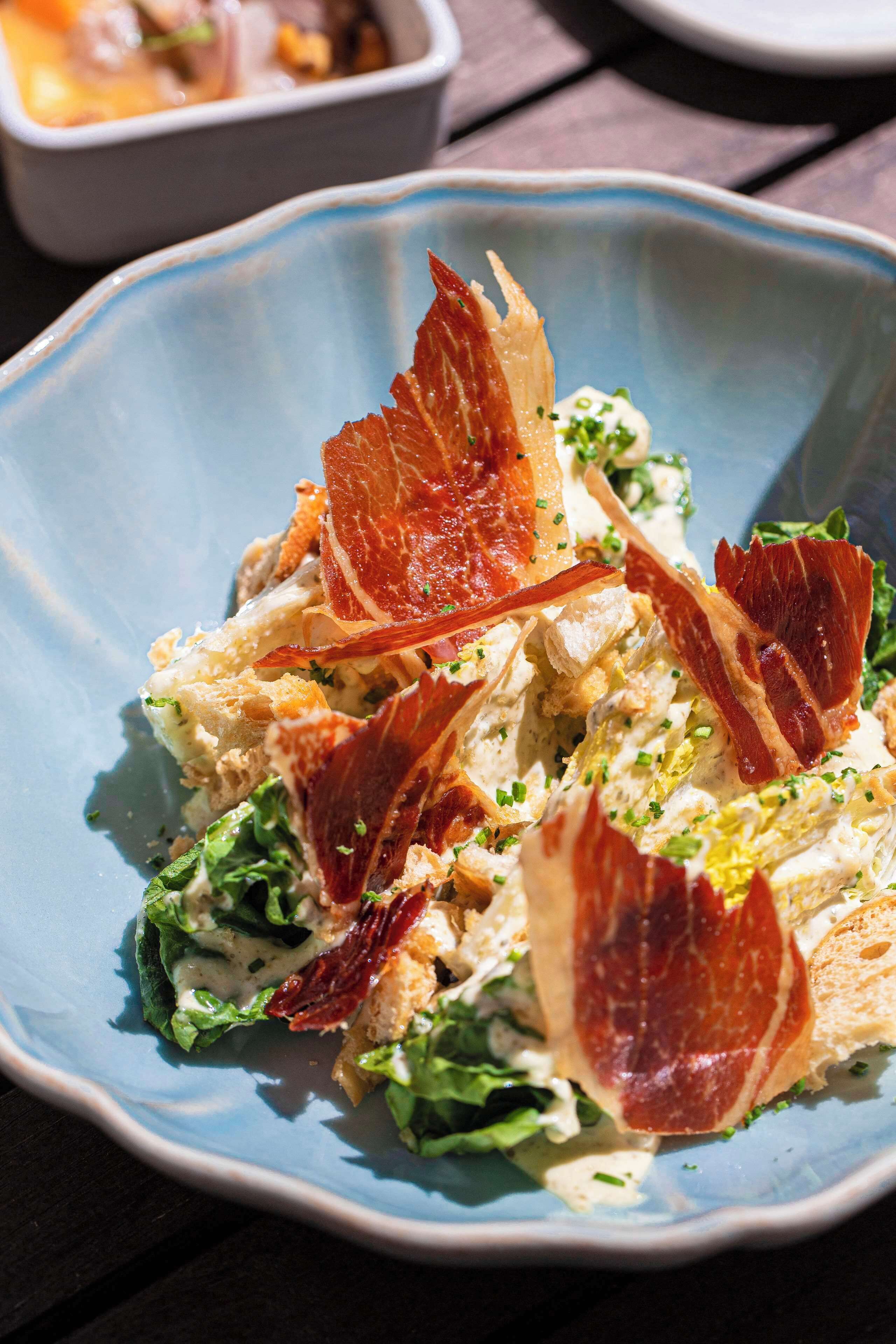 A blue plate with a salad containing lettuce, croutons, and bacon.