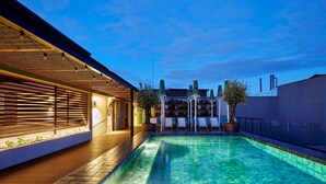 A swimming pool with lounge chairs and umbrellas, surrounded by a building with a covered patio and a view of the city skyline. - Radisson Blu 1882 Hotel, Barcelona Sagrada Familia (Barcelona)