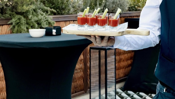 A table with a tray of drinks and a bowl, set against a backdrop of a building with spires. - Radisson Blu 1882 Hotel, Barcelona Sagrada Familia (Barcelona)