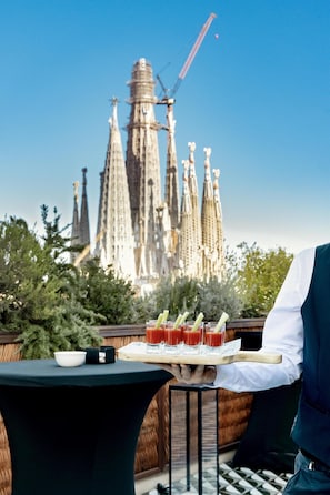 A table with a tray of drinks and a bowl, set against a backdrop of a building with spires. - Radisson Blu 1882 Hotel, Barcelona Sagrada Familia (Barcelona)