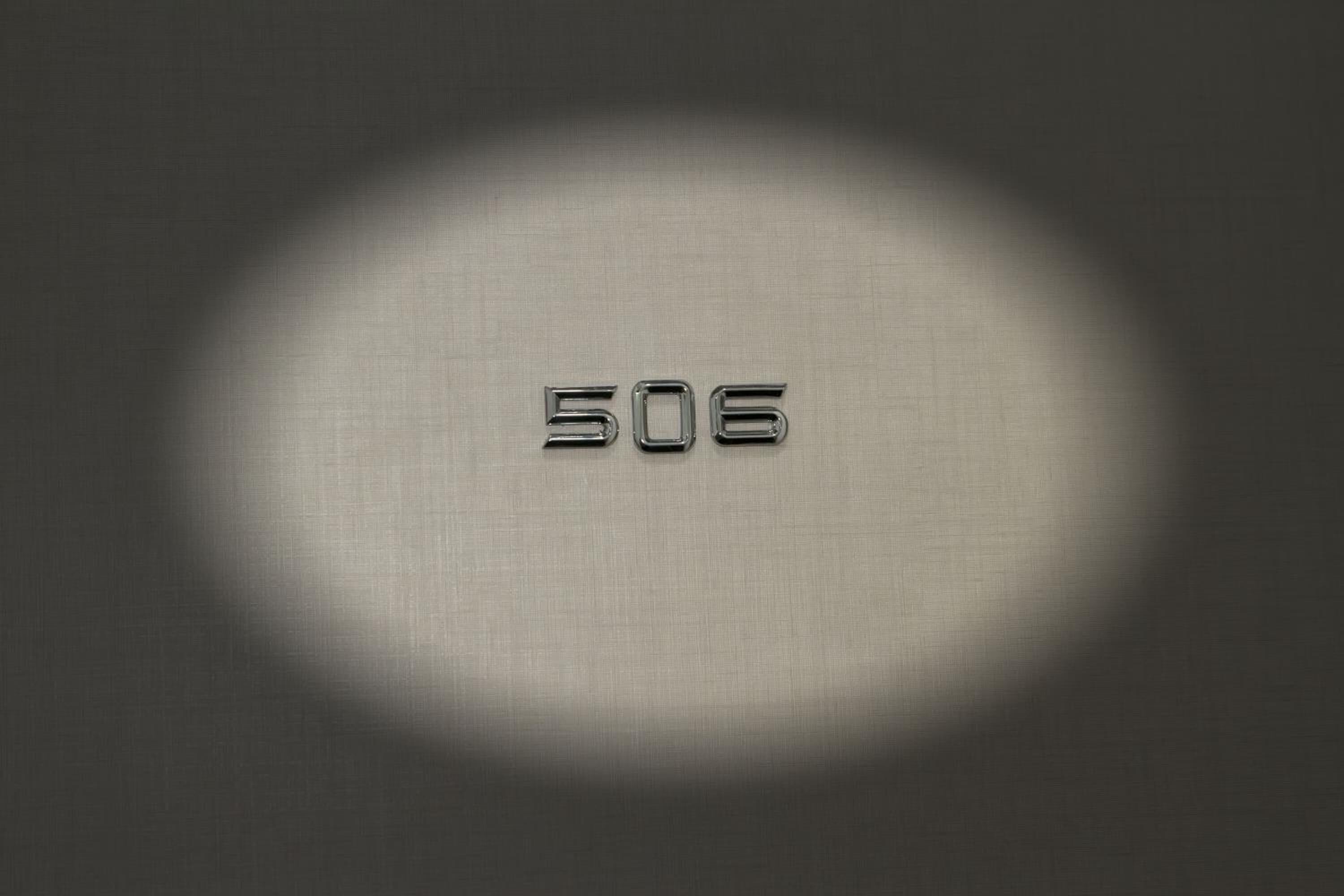 Een metalen nummer '506' verlicht door een spot op een structuur oppervlak.