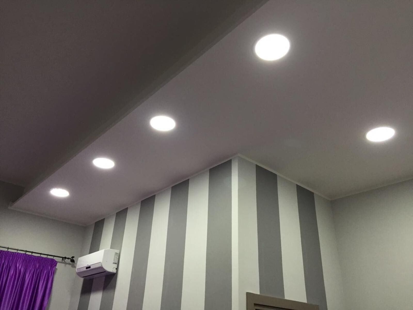 A bathroom with striped walls, a purple shower curtain, and a ceiling with recessed lighting.