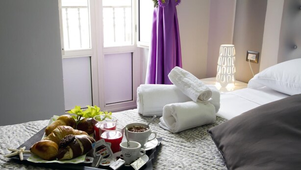 Una cama bien hecha con sábanas blancas, una bandeja con cruasanes, café y jugo, y una lámpara de noche.