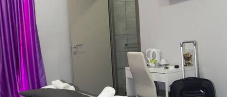 A hotel room with a bed, a desk with a chair, a suitcase, and a TV on the wall.